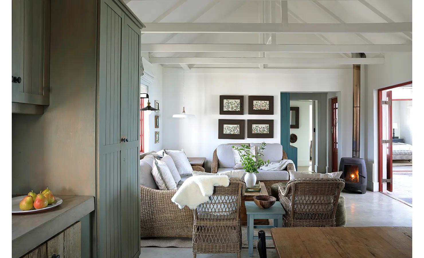 Perfect Hideaways: A cosy living room styled in soft neutrals with wicker furniture, botanical prints, and a wood-burning stove, creating a serene space that blends comfort with rustic charm. Churchhaven, Fynbos.