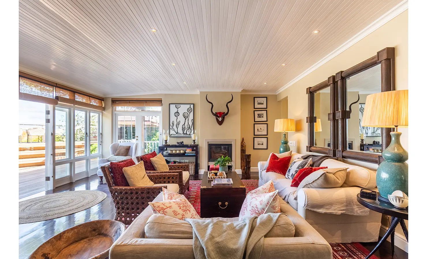 Perfect Hideaways: A stylish corner of the living space, featuring elegant white armchairs, zebra-print accents, and a scenic view of the ocean through French doors. Dolphin Cottage, Camps Bay.