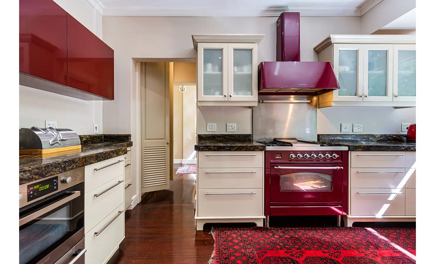 Perfect Hideaways: A contemporary kitchen with sleek cabinetry, a deep red stove, and dark granite countertops, blending modern convenience with timeless style. Dolphin Cottage, Camps Bay.