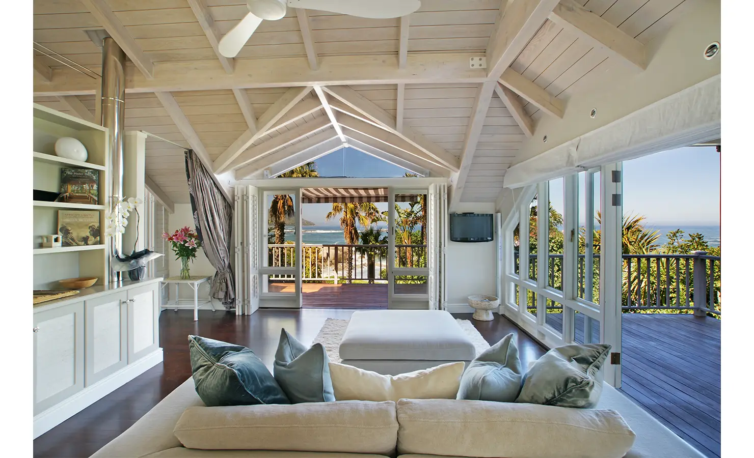 Perfect Hideaways: A dreamy living space with an elegant fireplace, built-in bookshelves, and expansive glass doors opening to a deck with breathtaking sea views. Dolphin Cottage, Camps Bay.