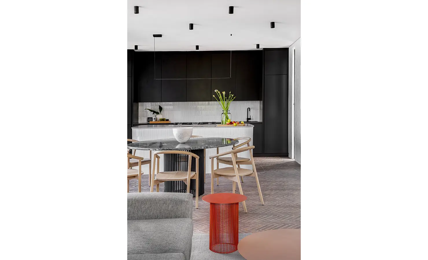 Perfect Hideaways: A sleek open-plan kitchen showcases matte black cabinetry, a curved white-tiled island, and light wooden dining chairs around a glossy black table. STIL, Montagu.