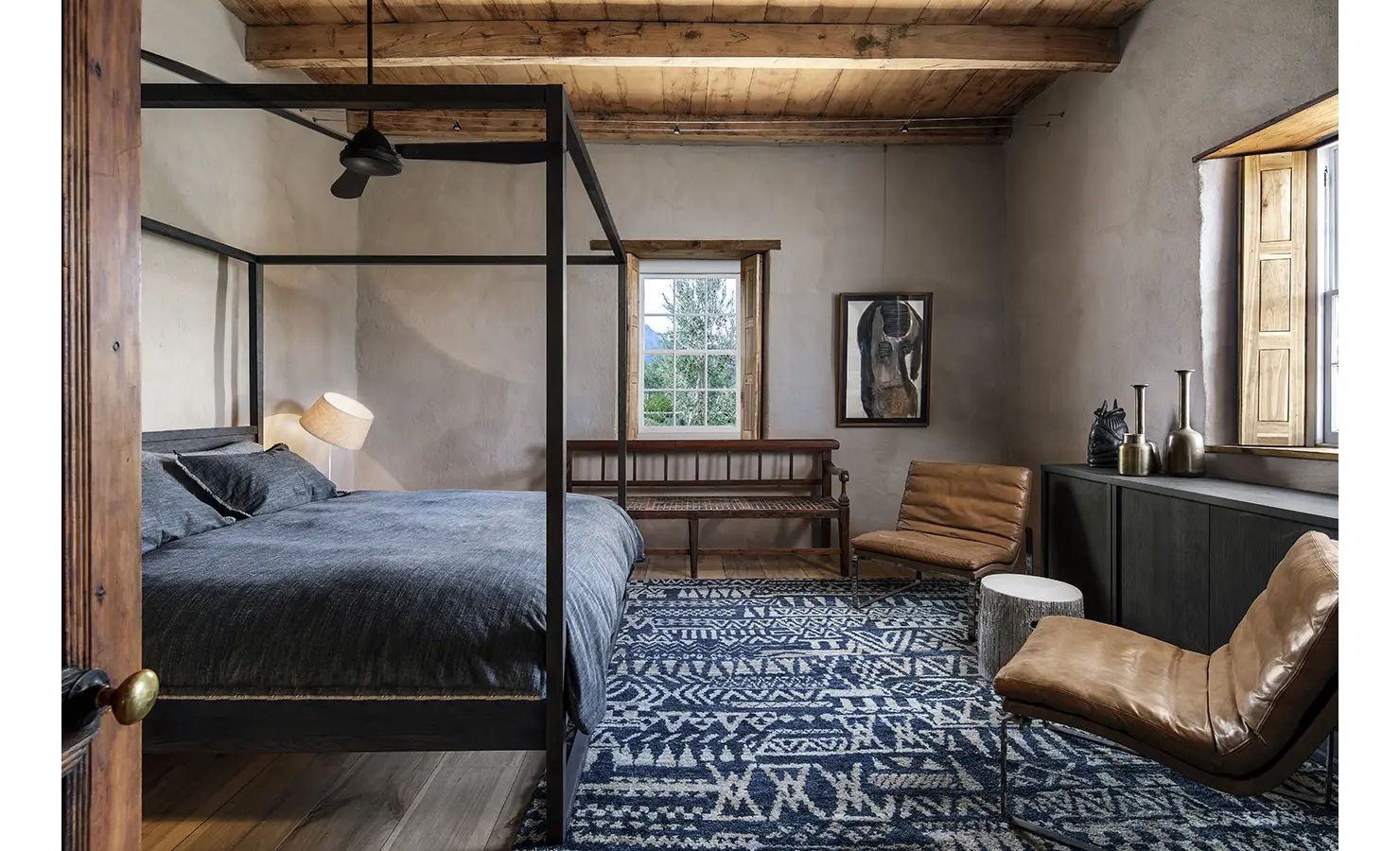 Perfect Hideaways: Moody bedroom with four-poster bed, patterned blue rug and tan leather loungers beneath timber beams, Ladismith, Buffelsdrift