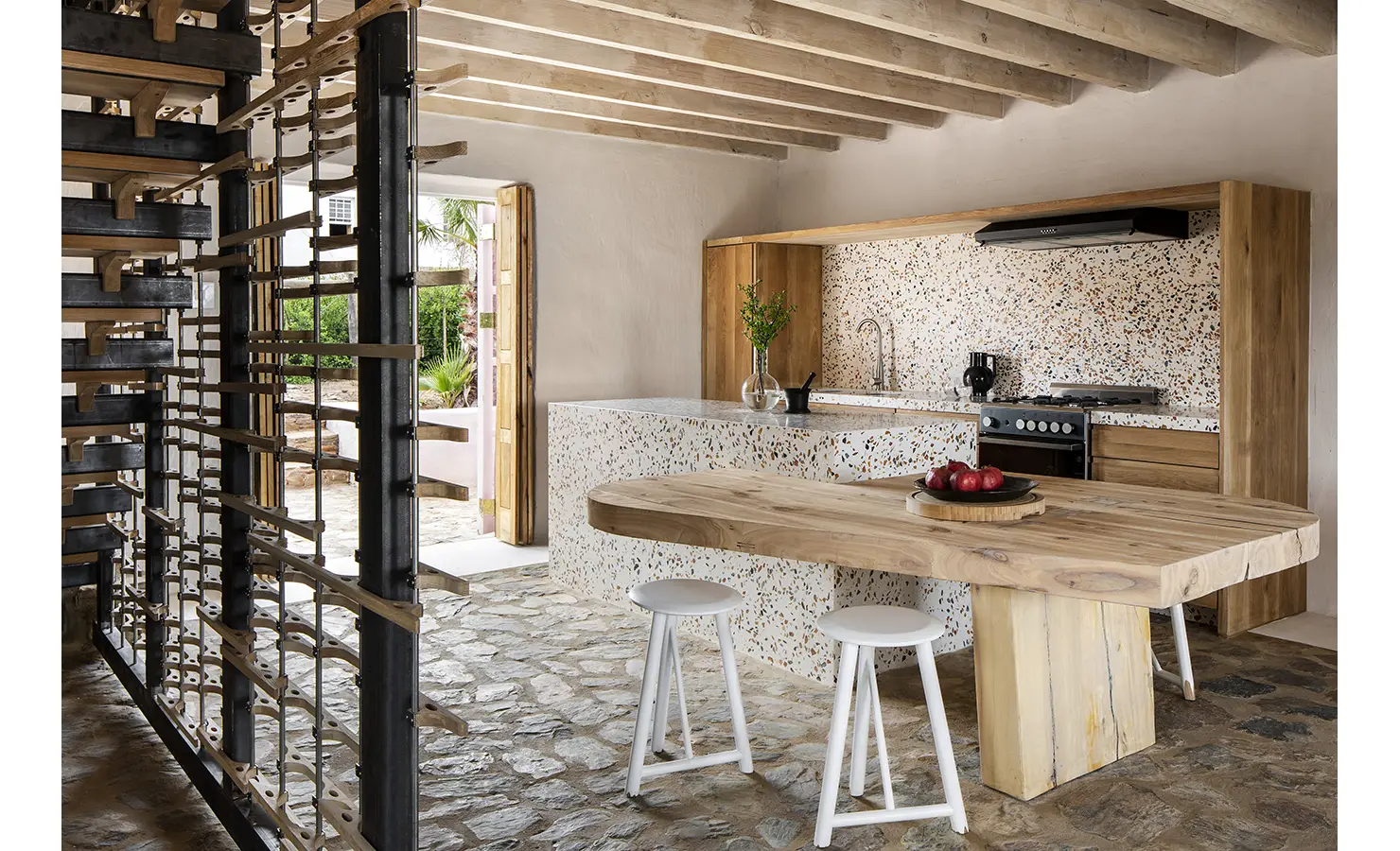 Perfect Hideaways: Terrazzo-clad kitchen with chunky timber dining table and stools, stone floor and steel-timber wine rack, Ladismith, Buffelsdrift