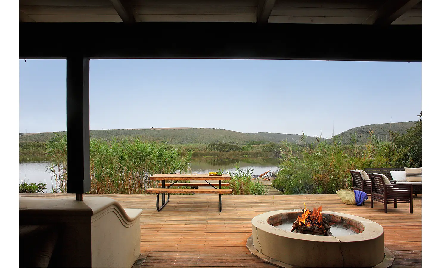 Perfect Hideaways: A covered outdoor lounge area featuring a firepit, a wooden deck, and scenic views of the river and surrounding vegetation. Breede Riverhouse 327, Malgas.