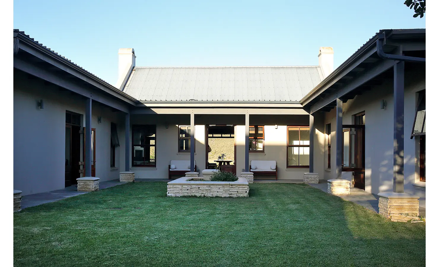 Perfect Hideaways: A courtyard with lush green grass, framed by symmetrical architectural lines and cosy seating areas. Breede Riverhouse 327, Malgas.