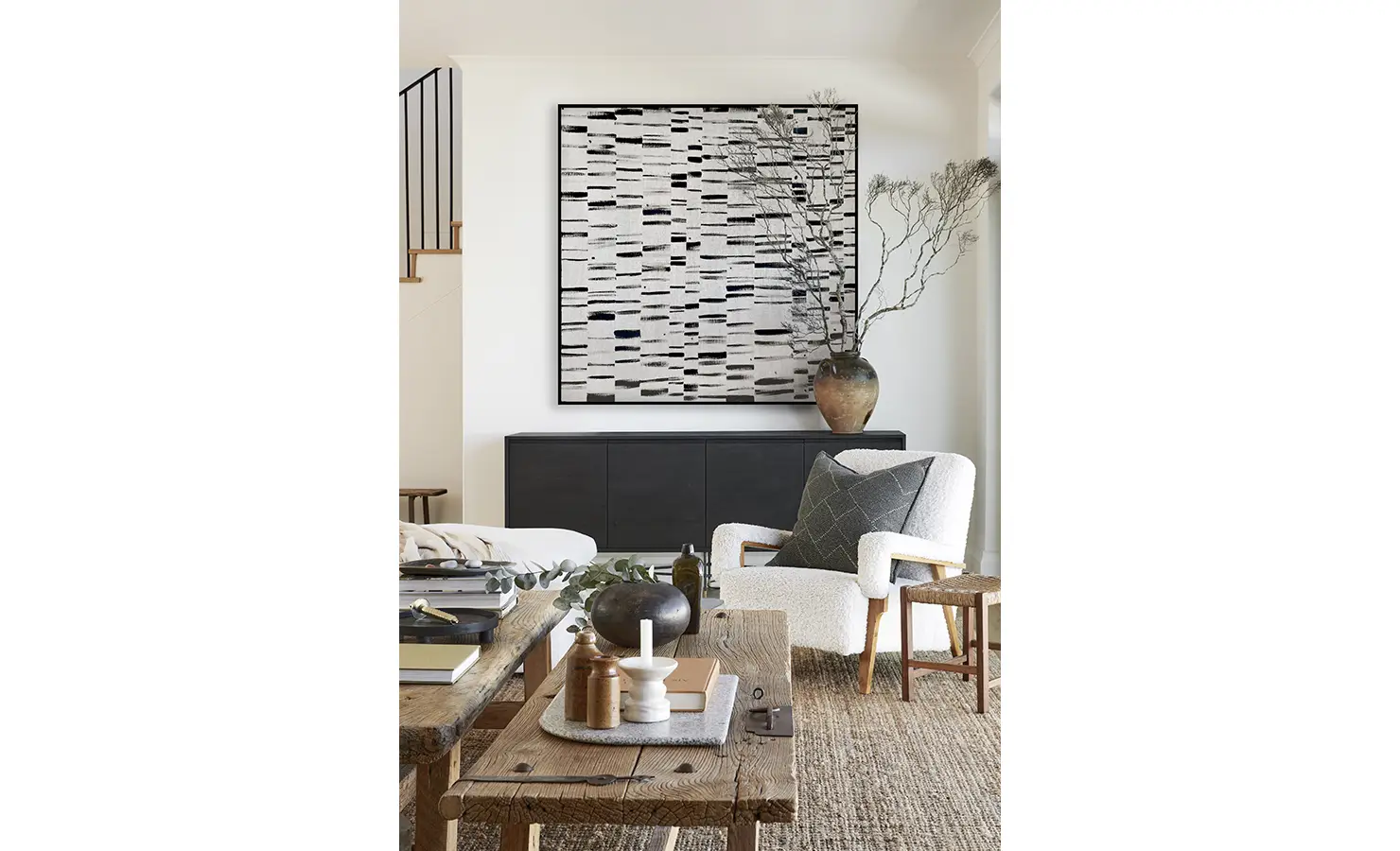 Perfect Hideaways: A cosy reading corner features a boucle armchair, rustic wood furnishings, and abstract monochrome artwork that adds a bold focal point to the neutral-toned space. Sophie's Rock, Hermanus.