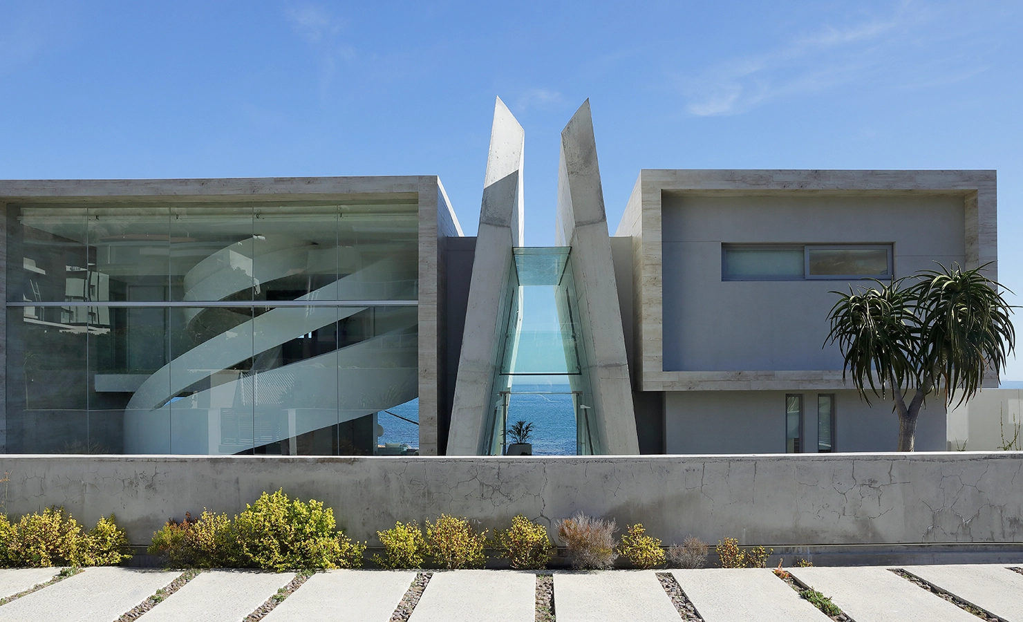 Perfect Hideaways: Striking contemporary architecture with dramatic angular forms and expansive glass walls frames uninterrupted ocean views, featuring a sculptural spiral staircase and minimalist landscaping. Bahari, Llandudno.