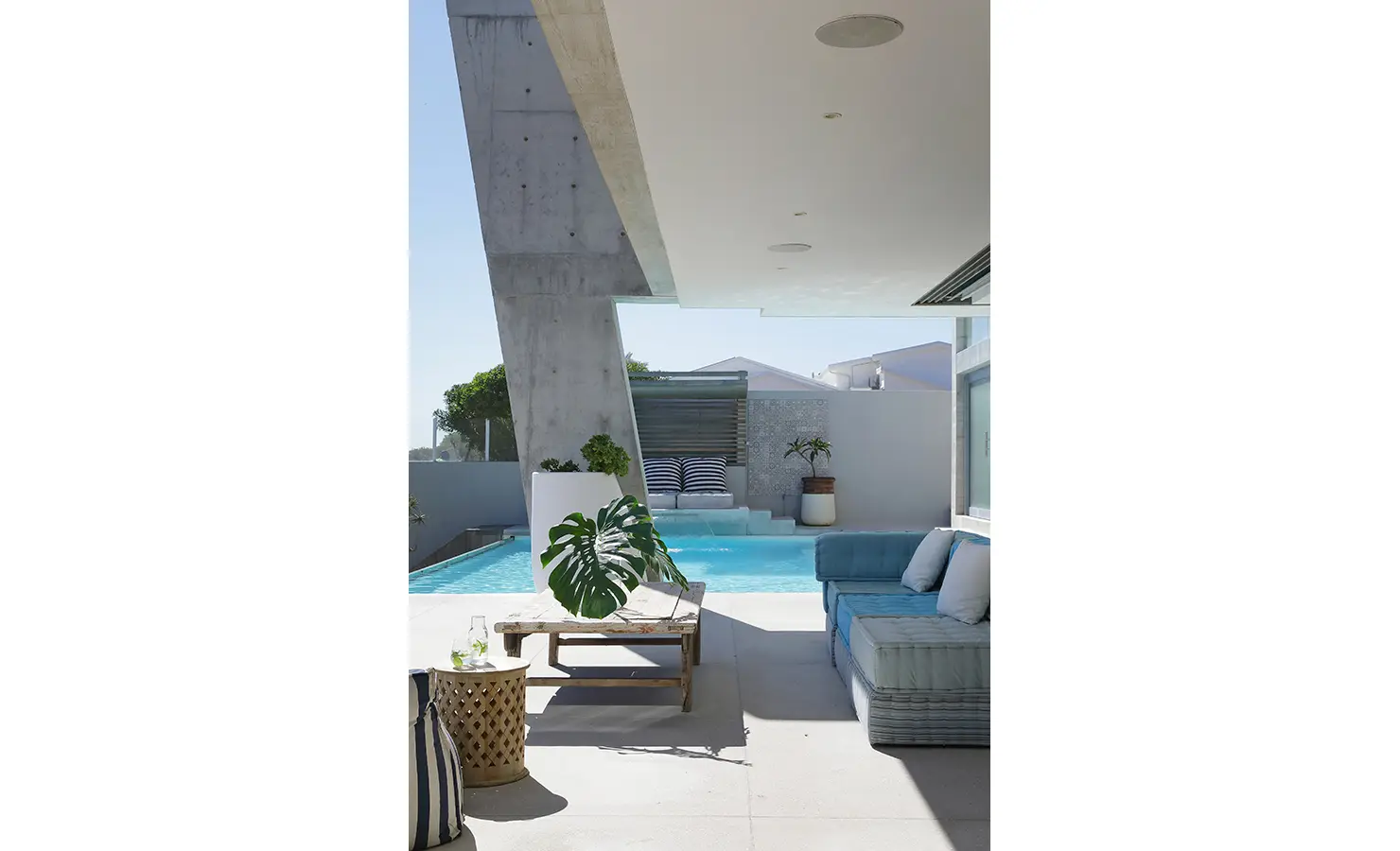 Perfect Hideaways: A shaded outdoor seating area with plush blue cushions and a view across the pool to a sunlit daybed nook, perfect for relaxed coastal living. Bahari, Llandudno.
