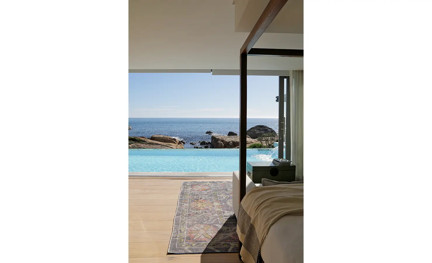 Perfect Hideaways: A chic, shaded daybed with striped cushions overlooks an infinity pool and the ocean, blending luxury with nature in a beautifully designed outdoor nook. Bahari, Llandudno.