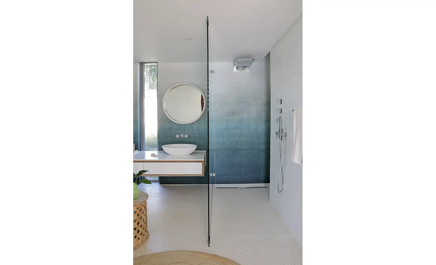 Perfect Hideaways: A minimalist bathroom with a walk-in shower and striking ombré blue wall, complemented by a round mirror, floating vanity, and clean lines. Bahari, Llandudno.