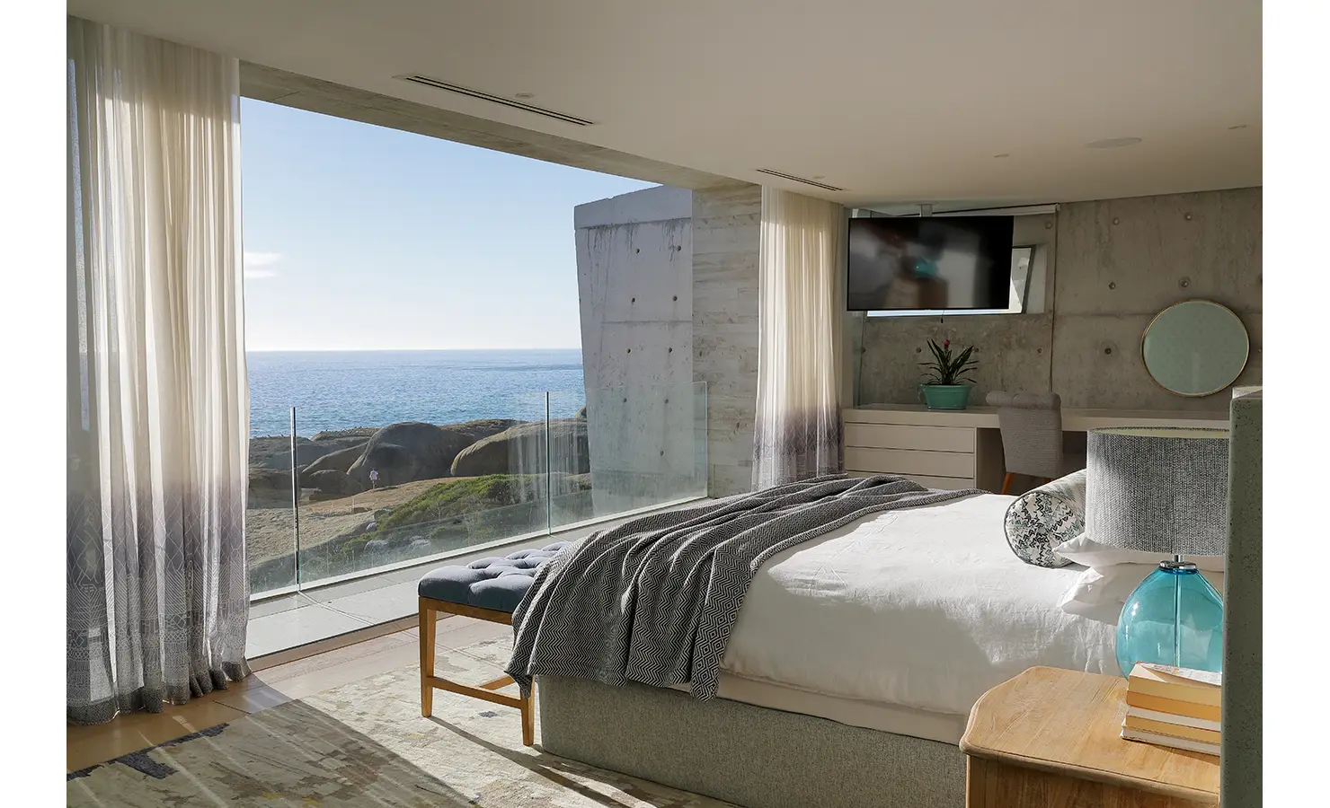 Perfect Hideaways: A serene bedroom featuring a four-poster bed, neutral tones, and a soft loveseat, framed by warm wooden accents and a richly textured rug. Bahari, Llandudno.