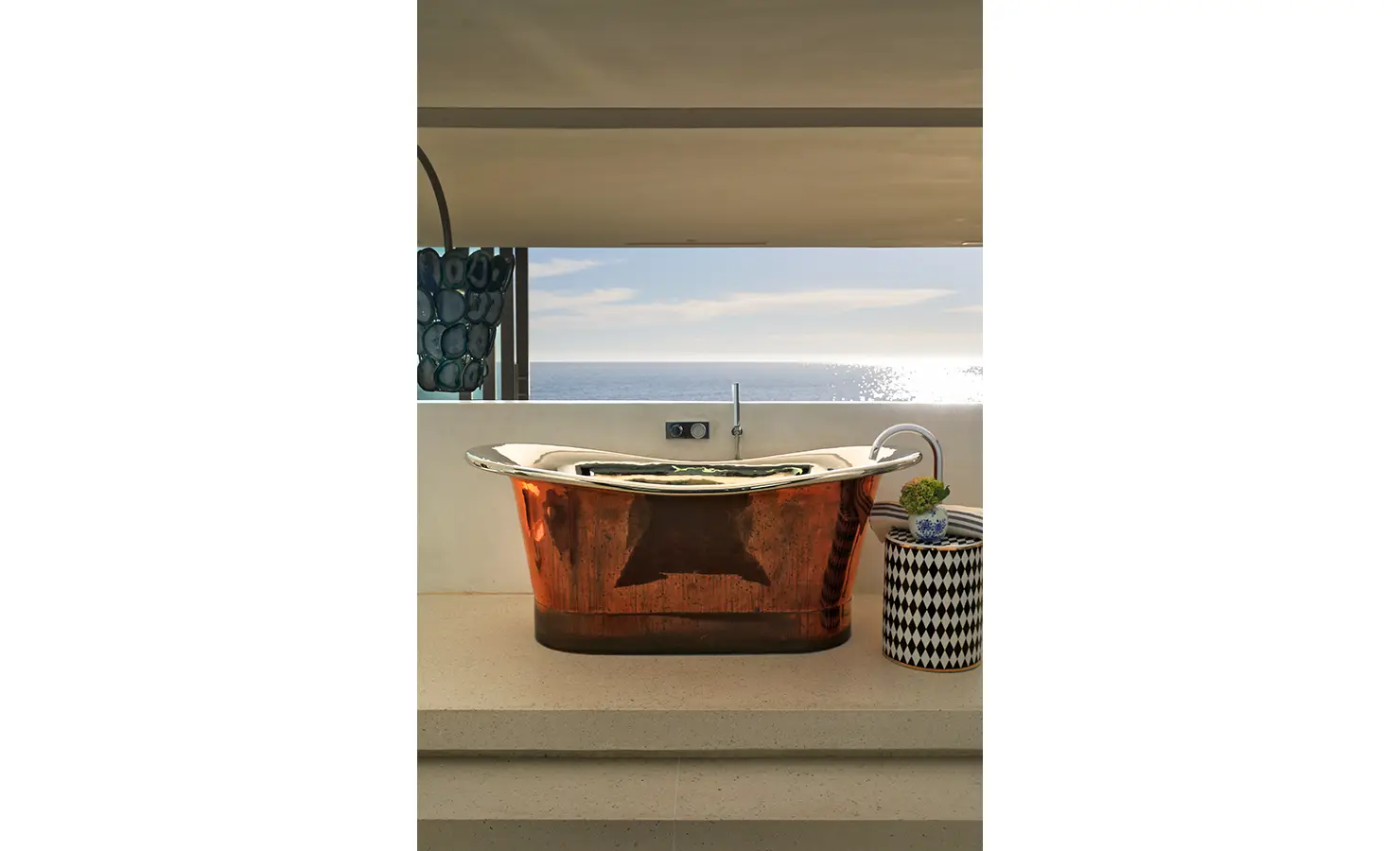 Perfect Hideaways: A gleaming copper bathtub positioned to soak in uninterrupted ocean views, paired with playful patterned side tables and elegant finishes. Bahari, Llandudno.