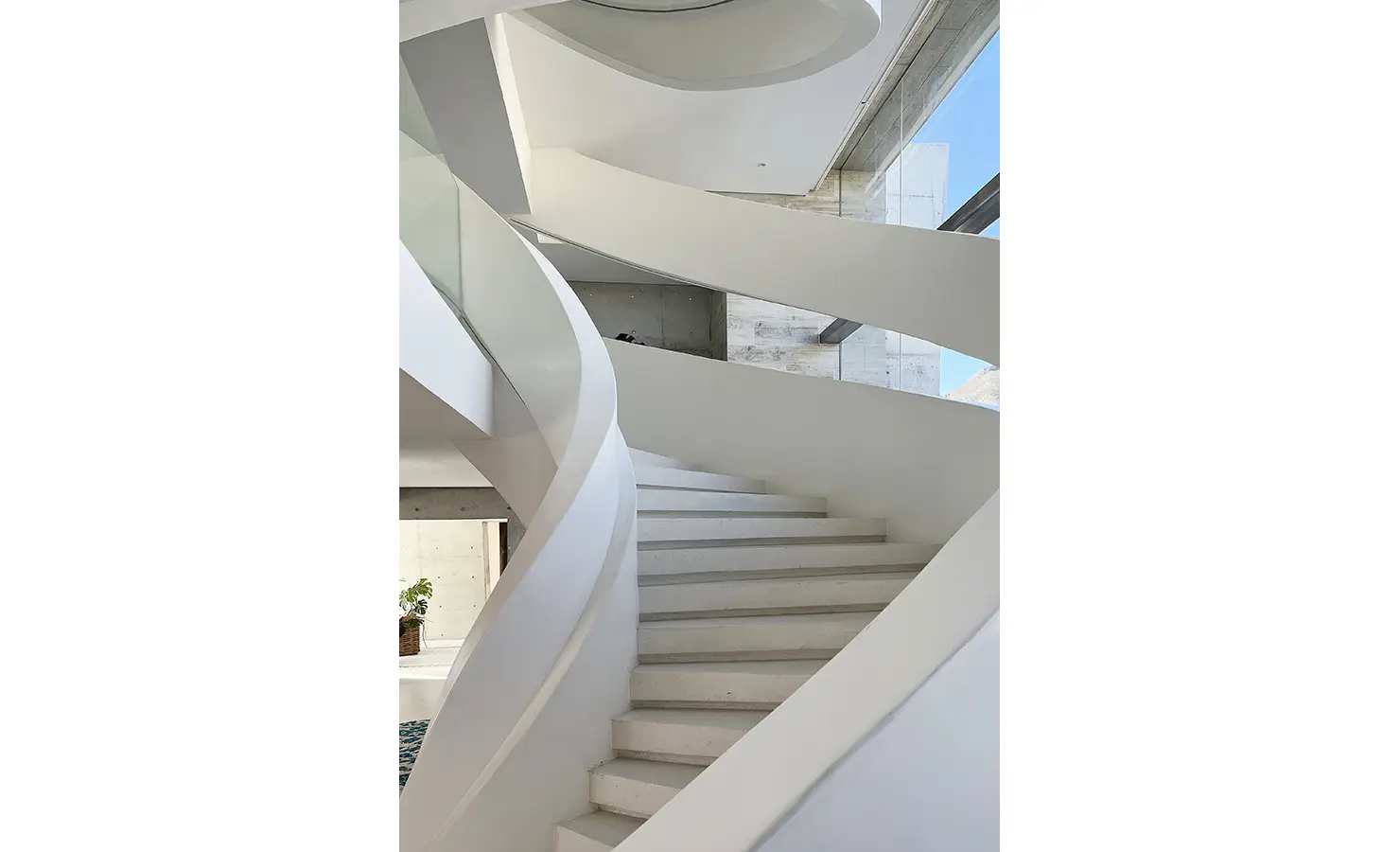 Perfect Hideaways: A dramatic sculptural staircase winds upward in smooth white curves, bathed in natural light from floor-to-ceiling windows. Bahari, Llandudno.