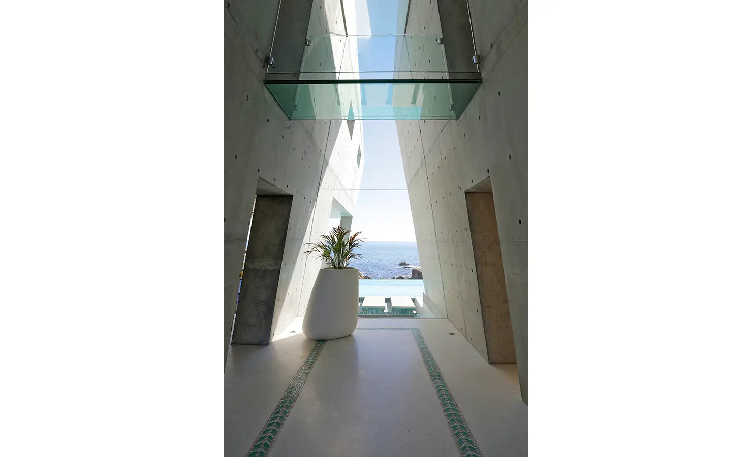 Perfect Hideaways: A striking architectural walkway with angled concrete walls and a suspended glass bridge frames a panoramic view of the ocean beyond. Bahari, Llandudno.
