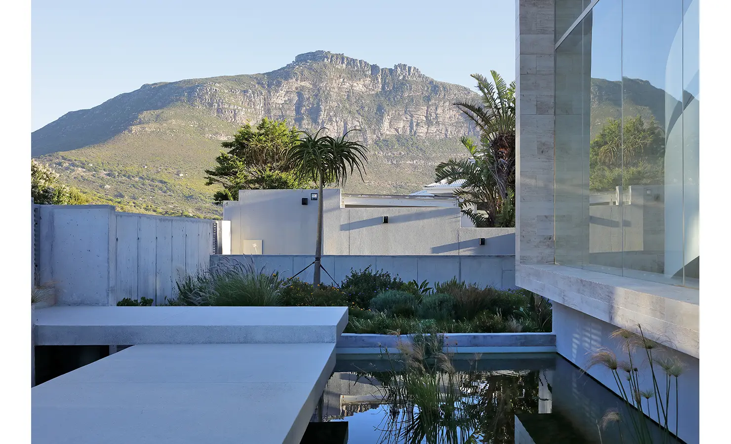 Perfect Hideaways: A tranquil courtyard scene with reflective water features, lush indigenous planting, and majestic mountain views rising in the background. Bahari, Llandudno.