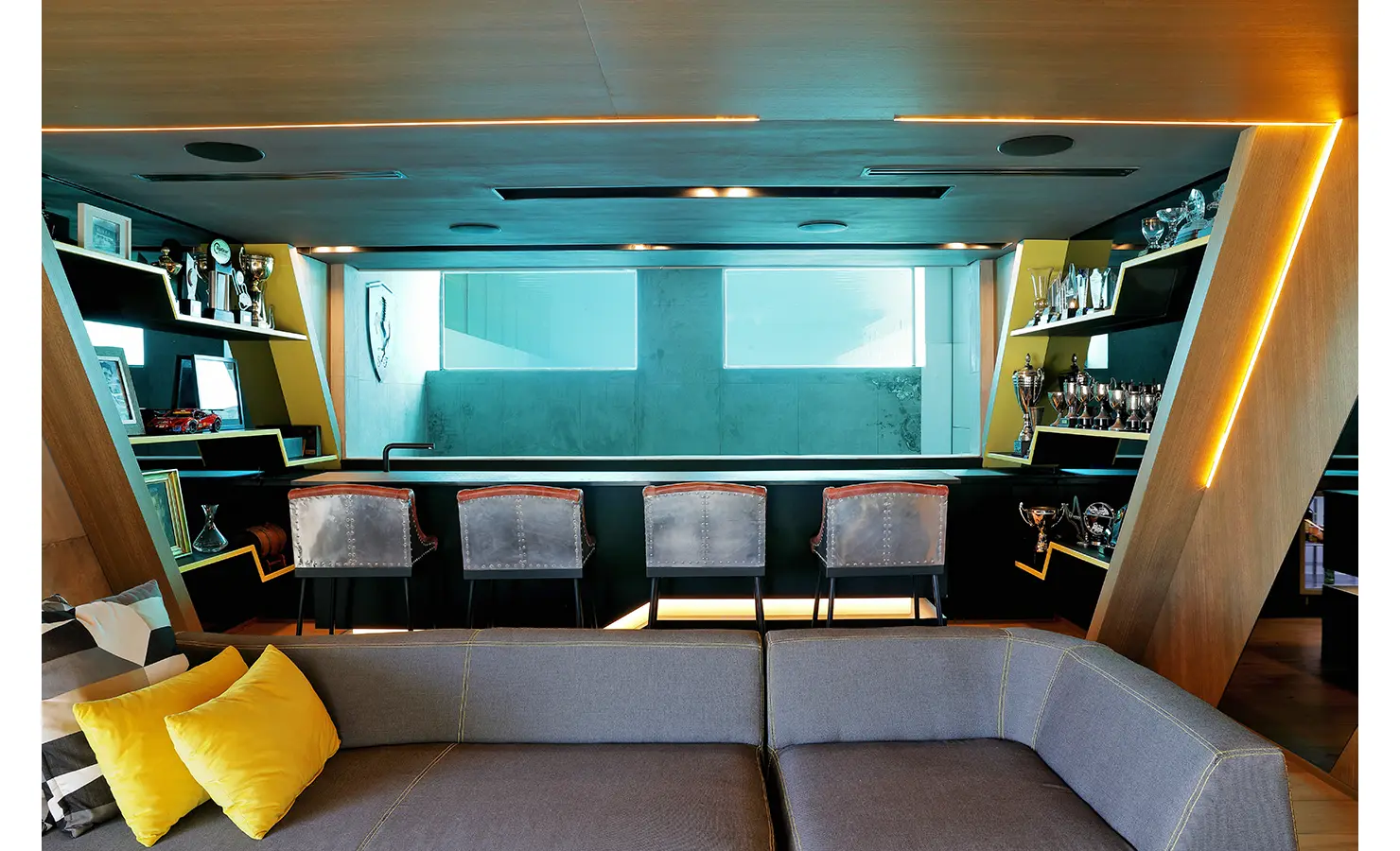 Perfect Hideaways: A moody, luxurious entertainment space with a bar overlooking an underwater pool window, surrounded by shelves of trophies and ambient lighting. Bahari, Llandudno.