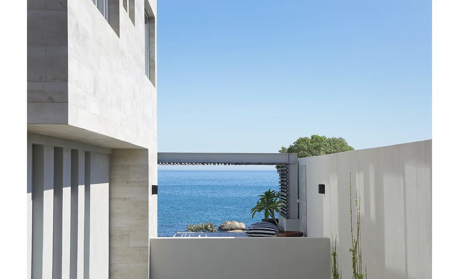 Perfect Hideaways: A peaceful exterior terrace tucked between modern concrete walls, with plush striped cushions and lush greenery opening to a spectacular sea view. Bahari, Llandudno.