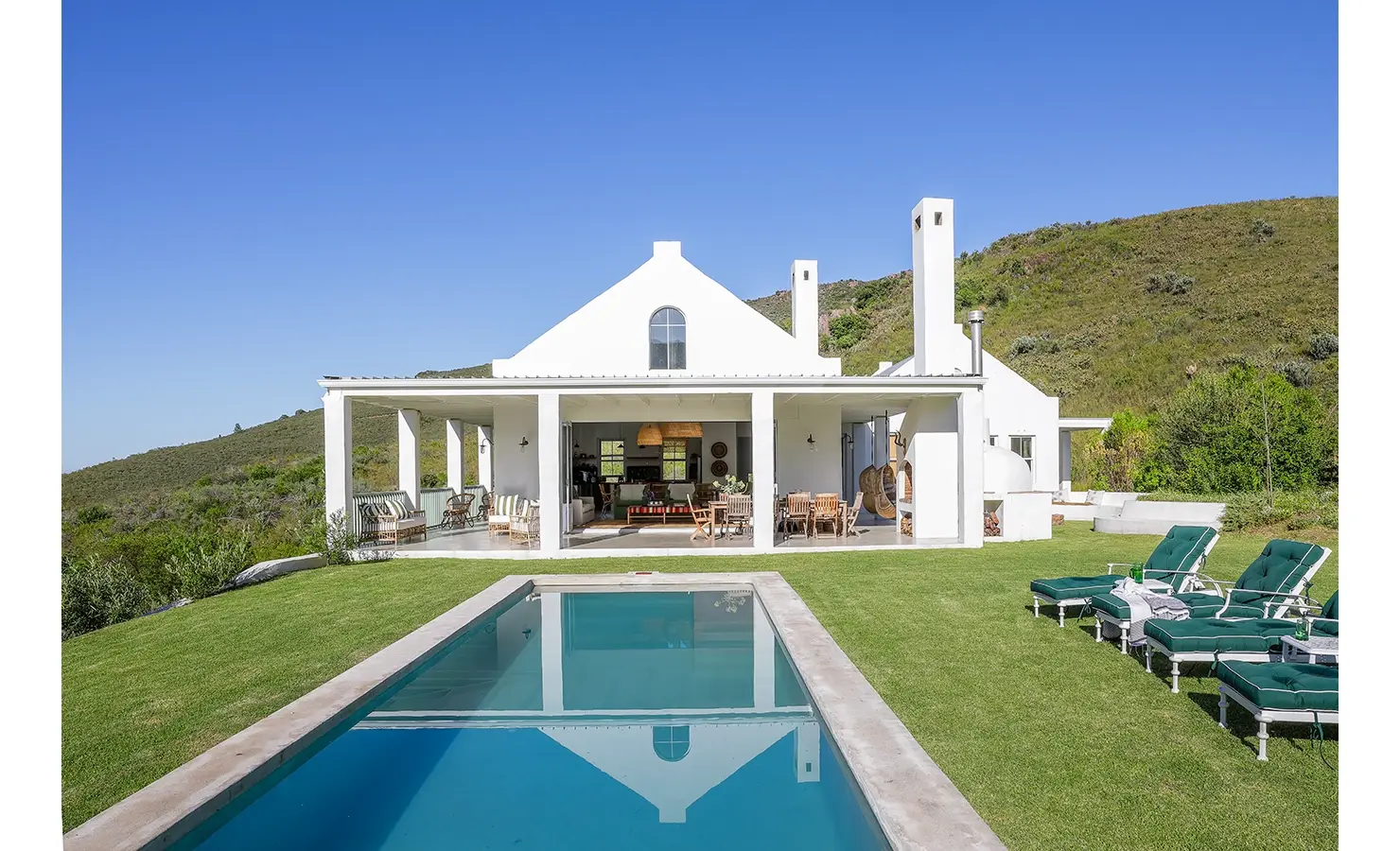 Extensive swimming pool in the garden facing Buchubos Villa with whitewashed walls and a wrap around verandah with large stack back doors, and surrounded by the natural landscape.