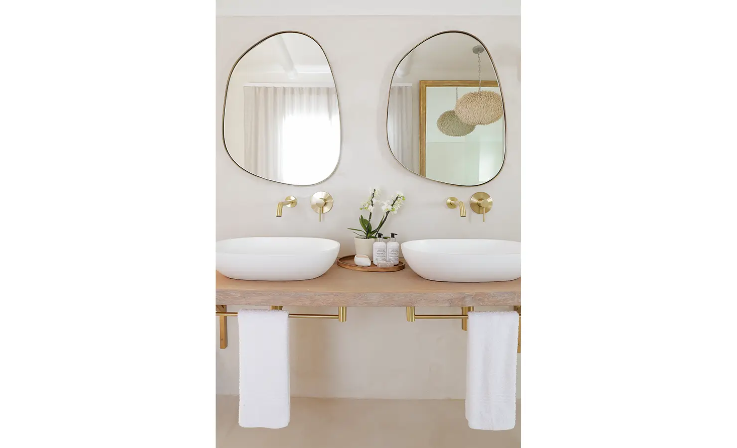 Perfect Hideaways: A chic double vanity bathroom features sculptural mirrors, brass fittings and elegant basin sinks set against a soft, neutral palette. Kinsail Beach Villa, Langebaan.