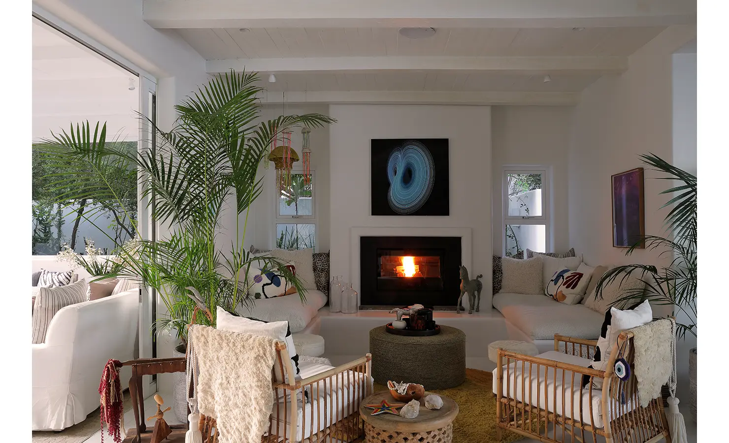 Perfect Hideaways: A snug living room with a lit fireplace, artistic decor, and comfortable seating surrounded by greenery, Ola Kala, Plettenberg Bay.