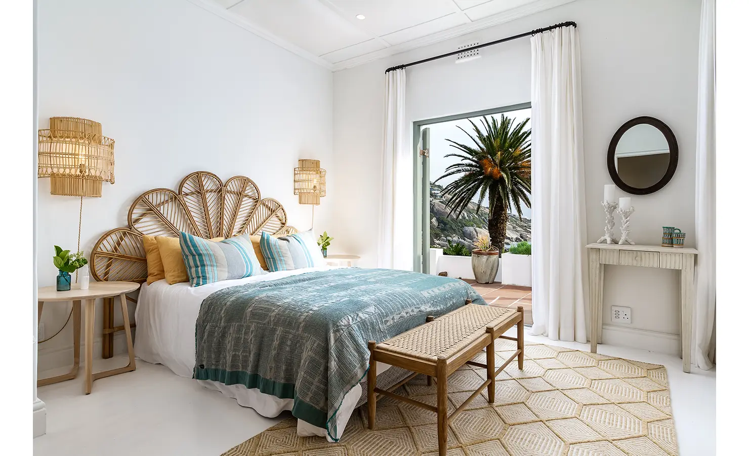 Bedroom with cane headboard, wooden side tables and bench with large blue bed throw and access to outdoors. Solmar.