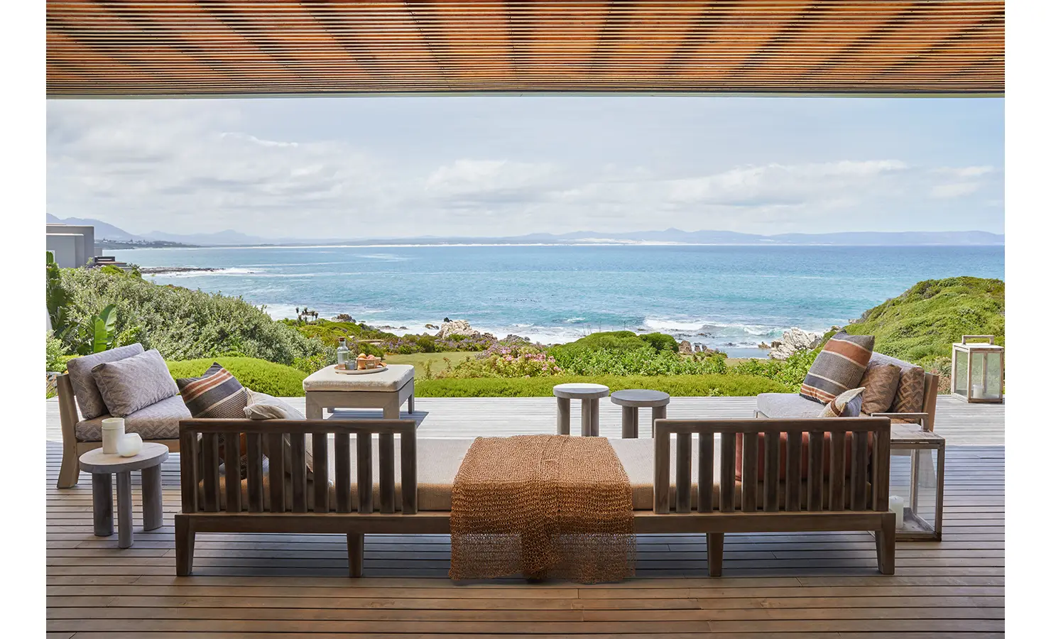 Covered outdoor deck area with large wooden bench seating looking out to garden and expansive sea views. Cliffside. Hermanus.