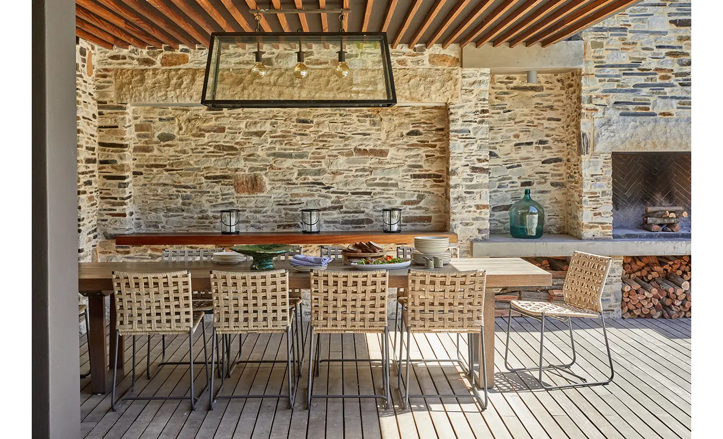 Covered deck area with stone wall, wooden table and chairs and fireplace. Cliffside. Hermanus.