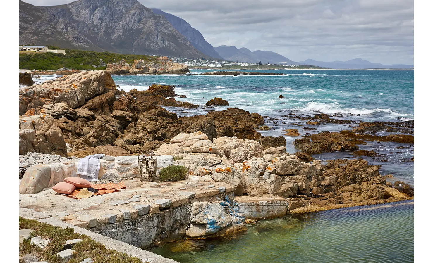 Rock pool leading out to blue and white seas, mountain views as the backdrop. Cliffside. Hermanus.