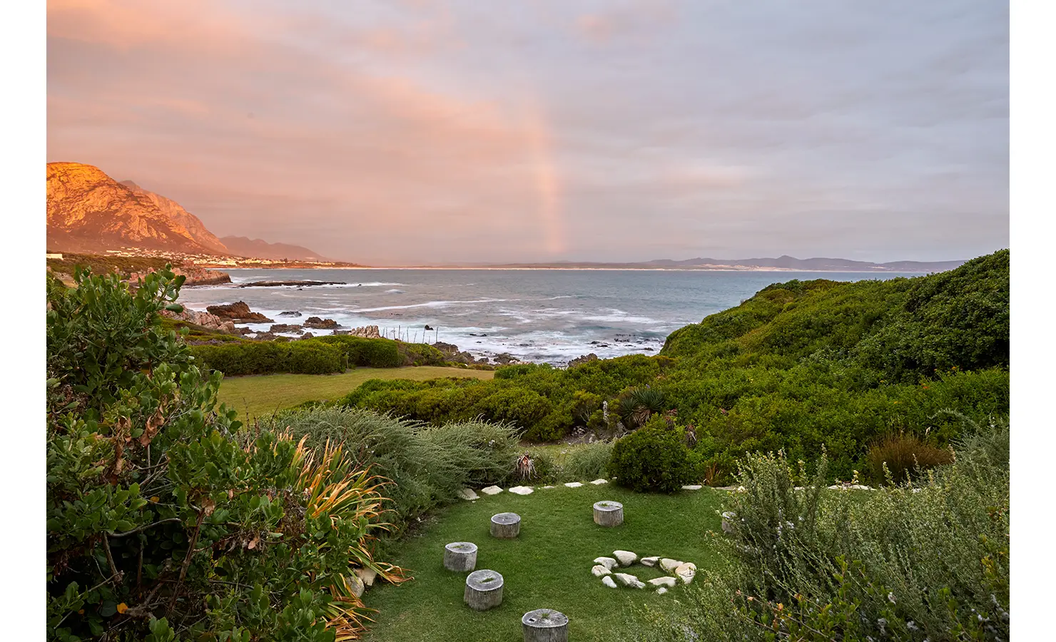 Rustic garden seating with views of ocean, mountain and orange sunset. Cliffside. Hermanus.