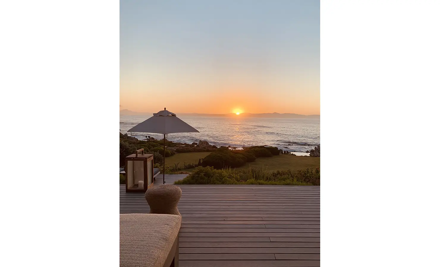 Outdoor deck area with umbrella and views of the ocean and orange sunset. Cliffside. Hermanus.