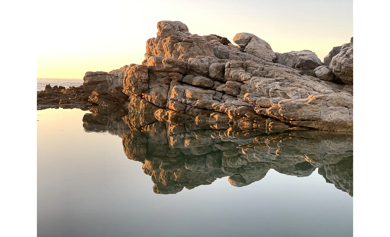 Still rock pool waters with sunset in the background. Cliffside. Hermanus.