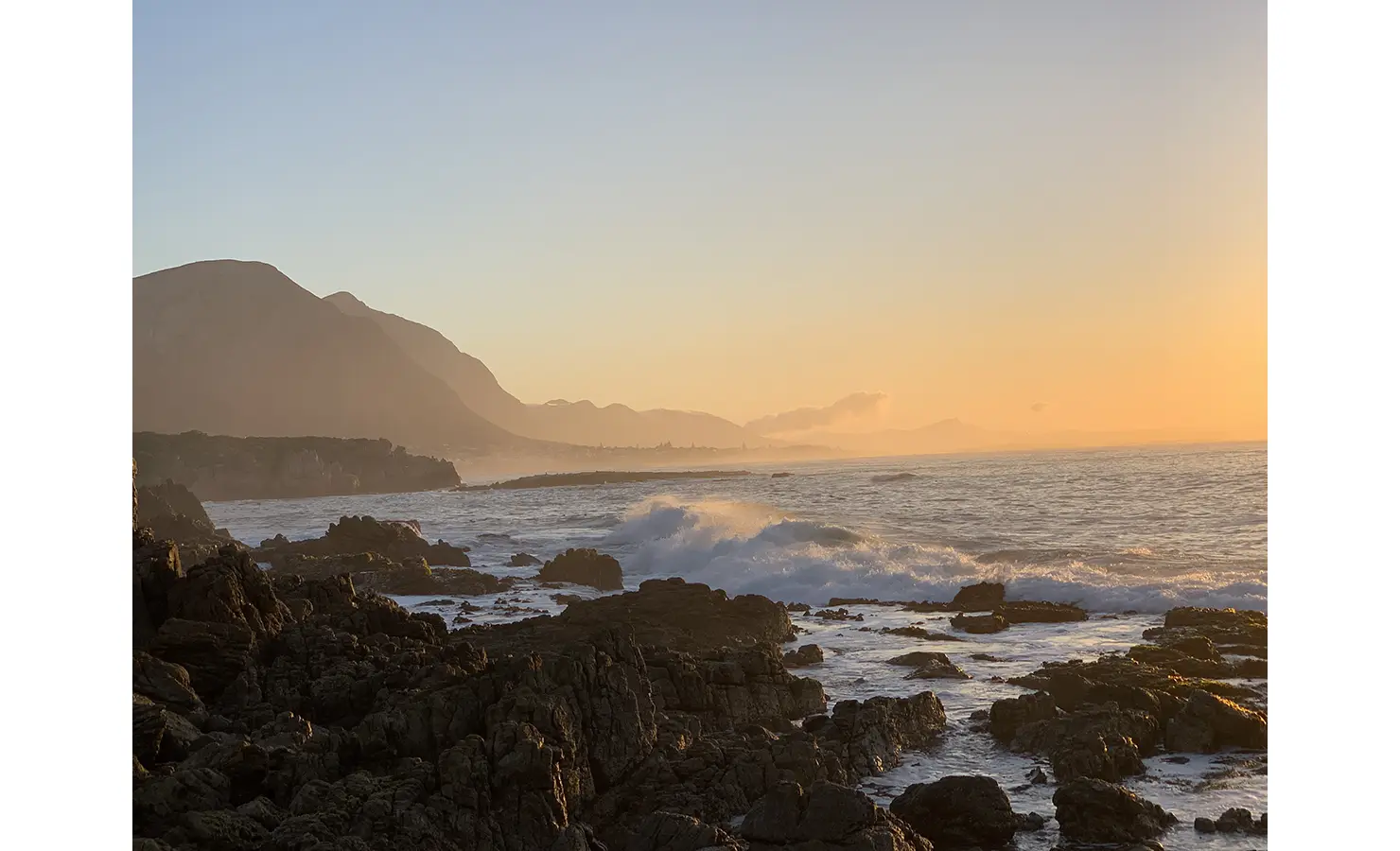 Rocks and crashing wave with ocean, mountain and sunset views. Cliffside. Hermanus.