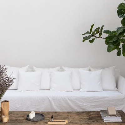 Calm and serene living area in Casa Piana with a large white linen sofa and soft white walls, a wooden coffee table with trinkets and a large corner pot plant.