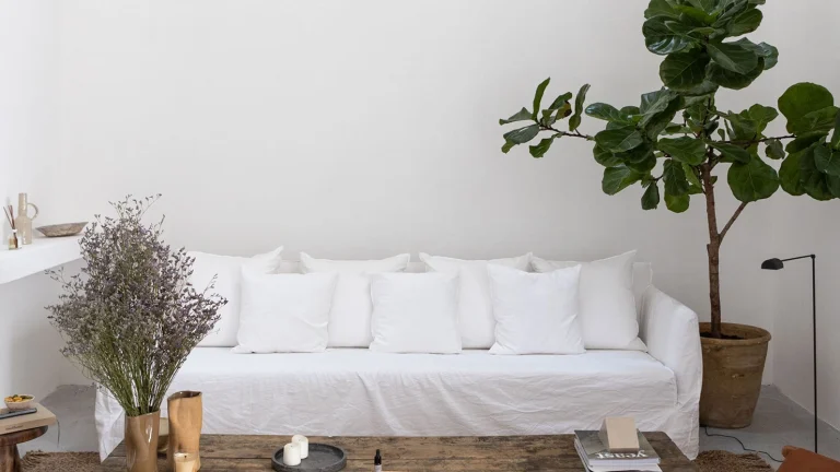 Calm and serene living area in Casa Piana with a large white linen sofa and soft white walls, a wooden coffee table with trinkets and a large corner pot plant.