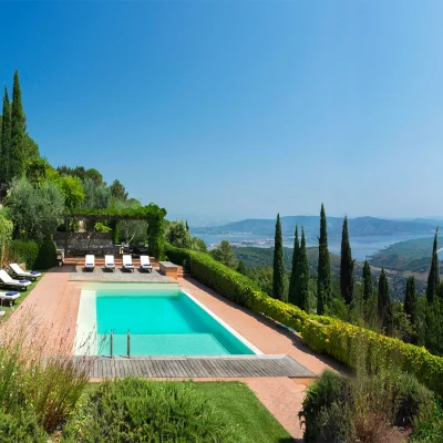 A large turquoise blue lap pool with wrap around red brick paving and a luscious green garden set in the midst of the forested slopes of Tuscany with panoramic views of the ocean and mountainous landscape. Villa Sunshine.