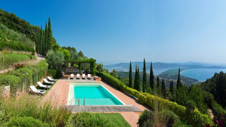 A large turquoise blue lap pool with wrap around red brick paving and a luscious green garden set in the midst of the forested slopes of Tuscany with panoramic views of the ocean and mountainous landscape. Villa Sunshine.