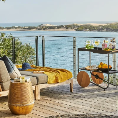 Wooden Deck situated on a river overlooking the ocean with two reclining loungers, a side table and drinks trolley.