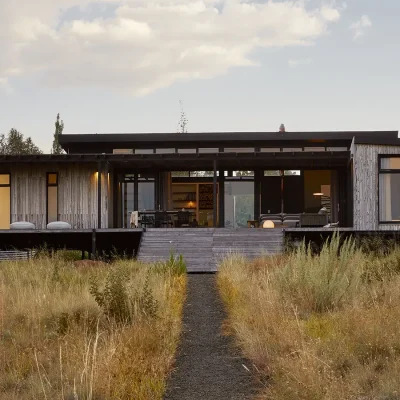 Contemporary farmhouse, the Herenberg with large stack back doors and windows opening onto a wooden patio facing the grassy plains and Maloti mountain range.