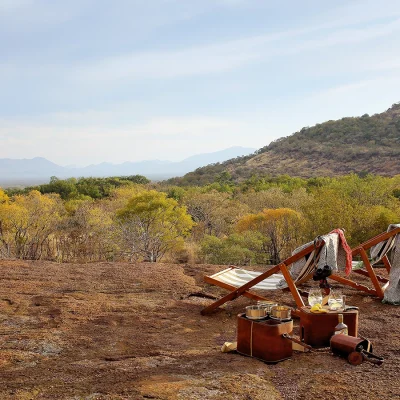 Wooden striped sun loungers positioned on an escarpment overlooking the bush terrain and distant mountains. Cypiro Leopard Lodge.