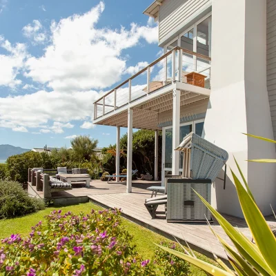 Pebbles, a beige clapboard home on the coast of Kommetjie with a wrap around verandah and green lawn.