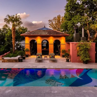 Green tropical garden with open pool house overlooking vibrant coloured pool. House Nouveau.