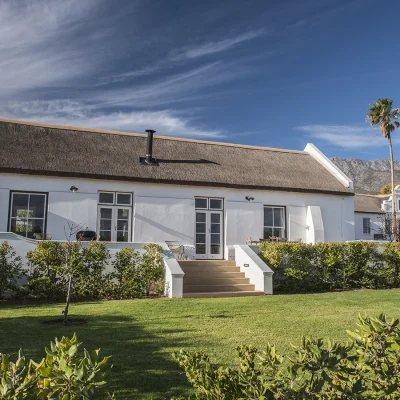 A white washed barn with thatched roof and rolling lawn with b.