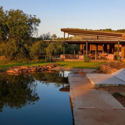 Natural swimming pool with reflections of Witklipfontein eco lodge, a modern structure with earth hues and a wrap around verandah overlooking the bushveld.