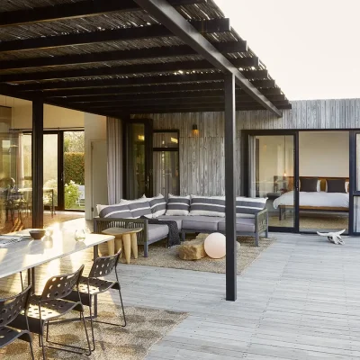 The Herenberg patio with a long, white granite dining table, an outdoor corner sofa and grey finish with a wooden slat pergola.