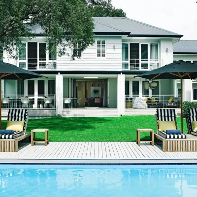 White cladded two story Atholplace House looking onto manicured green grass and a lap pool surrounded by blue and white striped sun loungers.