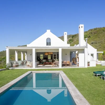 Extensive swimming pool in the garden facing Buchubos Villa with whitewashed walls and a wrap around verandah with large stack back doors, and surrounded by the natural landscape.