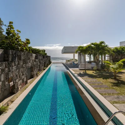 Lengthy lap pool surrounded by green lawn and an ocean view. Villa De L'Ocean.