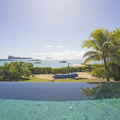 Infinity pool overlooking a luscious green lawn with palm trees and a sea view.