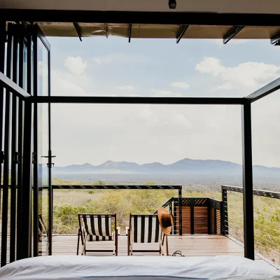 The View bedroom suite facing ceiling to floor stack back glass doors that open onto a wooden deck and the reserve with distant mountain ranges.