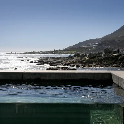 A contemporary swimming pool with a glass wall face sits perched on Ebb Tide's terrace overlooking Camps Bay ocean and mountain slopes.